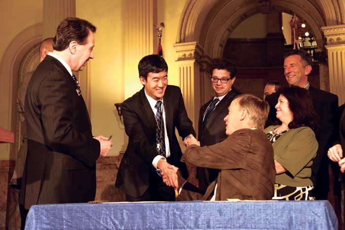 Dr. George Sam Wang and Gov. Hickenlooper shake hands and Wang receives the pen after signing the bill that moves toward a safer marijuana industry in Colorado.