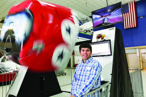 The MaxFlight Simulator rolls and pitches behind Ryan Gibbs, who shows visitors how to operate the controls.