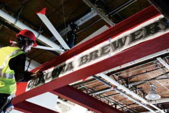 Painters prepare to put the Cheluna name on a ceiling beam at the entry to the brewery 