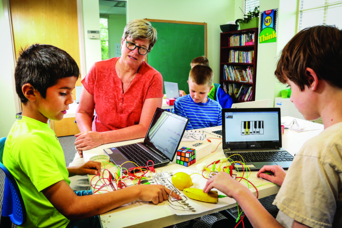 Brenda Lane, co-owner of eXL Learning Center at Lowry, which will open a spinoff called MindCraft in the Stanley Marketplace, helps some of her students studying electrical conductivity by using the lead from a pencil- the dots in the foreground - and fruits that can be part of a circuit that will play a short tune on the computer.