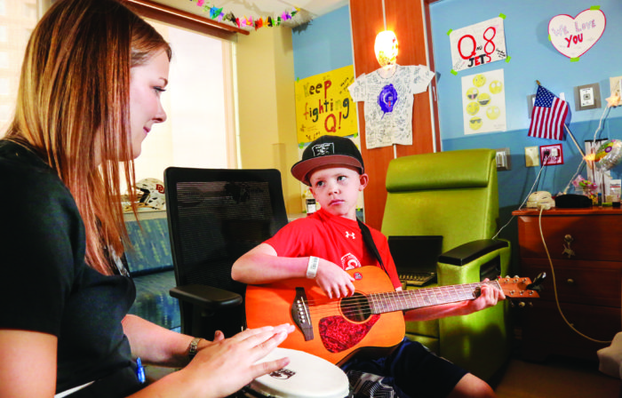 Music therapist Angela Wibben stops in to play a song with Quade, “Q” Marks in his room at Rocky Mountain Children’s Hospital.