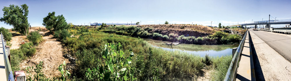 A new section of the Sand Creek Regional Greenway trail is being constructed under Smith Rd. and adjacent railroad bridges. In this wider-than-180-degree panorama view taken from Smith Rd. looking southwest, the roughed in trail is visible at left with Smith Rd. and the Central Park Blvd. bridge at right.