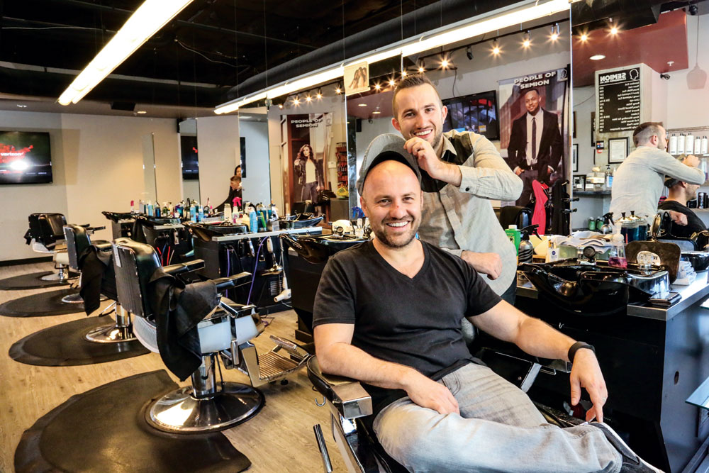 Roman Kikirov playfully tips his brother Simion’s cap revealing a mostly hairless head in their downtown Denver barber shop. The brothers plan to expand to Stanley Marketplace.