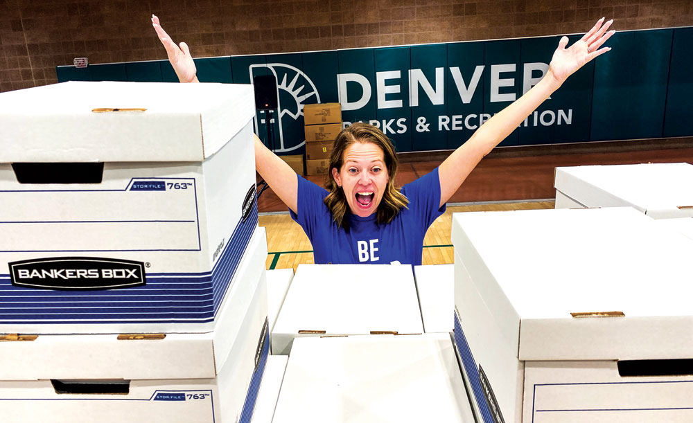 First Lady Courtney Johnston mugs for the camera from behind a stack of boxes filled with school supplies for Denver teachers. 