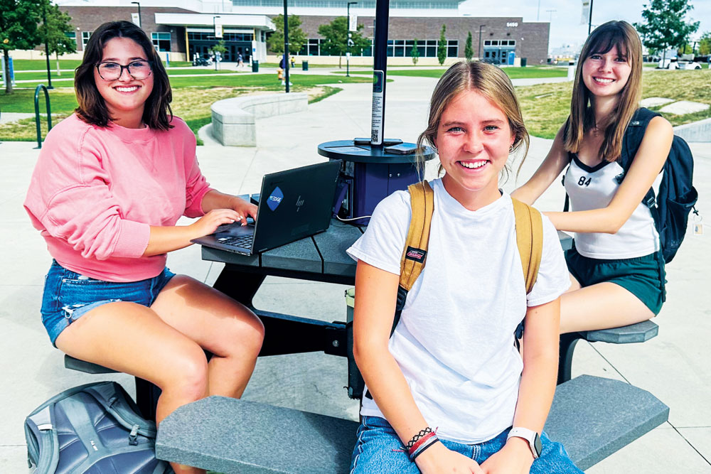 Maile McManis, Isadora Puckett, and Sofia Chaparro Will sit at one of the solar picnic tables that they wrote and won a grant for.